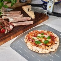En pizza med tomatsauce og basilikumblade ligger på en metalplade