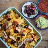 En rektangulær bageplade fyldt med nachos toppet med kylling