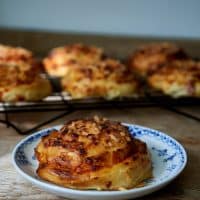 En nybagt bolle med smeltet ost ligger på en hvid tallerken med blå mønstre